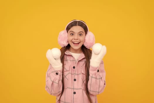 surprised kid in fur earmuffs playing snowballs on yellow background, winter.