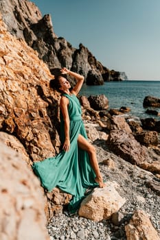 Woman green dress sea. Woman in a long mint dress posing on a beach with rocks on sunny day. Girl on the nature on blue sky background