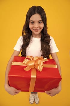 Happy teenager, positive and smiling emotions of teen girl. Teenager child in t shirt holding gift box on yellow isolated background. Gift for kids birthday. Summer holiday