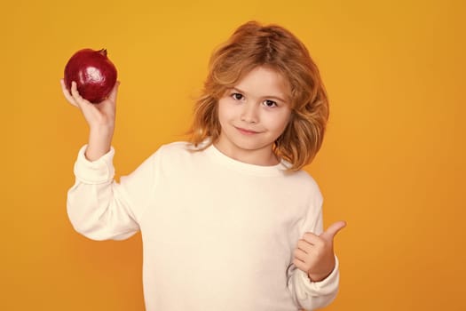 Kid hold red pomegranate in studio. Pomegranate fruit. Studio portrait of cute child with pomegranate isolated on yellow background