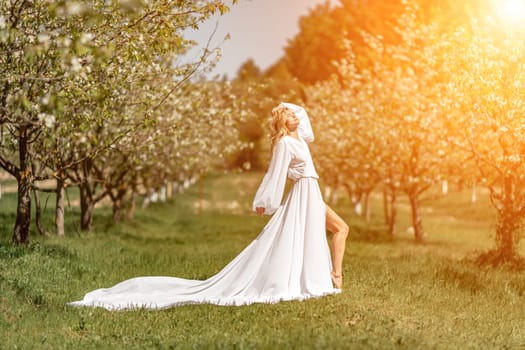 Blond blooming garden. A woman in a white dress walks through a blossoming cherry orchard. Long dress flies to the sides