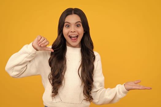 Excited teenager girl. Look at advert. Teenager child points aside shows blank copy space for text promo idea presentation, poses against yellow background