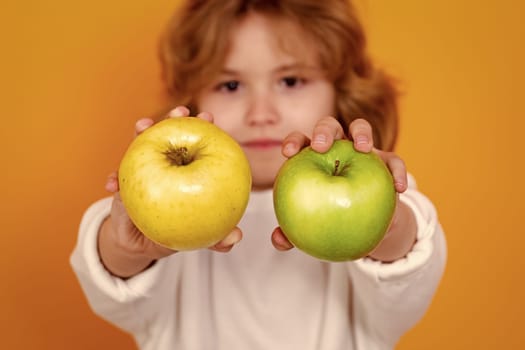 Kids face with fruits. Close up kid with apple in studio, selective focus. Studio portrait of cute child hold apple isolated on yellow background