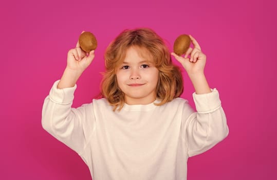 Kids face with fruits. Child hold kiwi in studio. Kiwi fruit. Studio portrait of cute kid boy with kiwi isolated on pink background