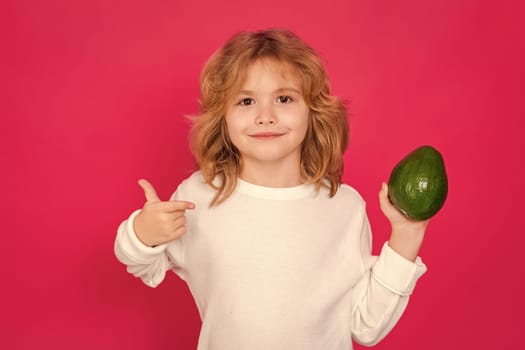 Kid hold red avocado in studio. Studio portrait of cute child with avocado isolated on red background