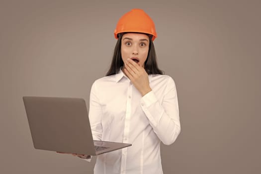 Surprised shocked excited business woman with laptop computer, portrait on gray. Young woman in helmet hold laptop computer on gray background. Architect businesswoman