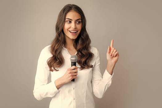 Woman speech, business woman holding a microphone. Young woman talking in microphone, perfom with mic, giving speech, standing on gray background