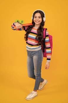 Teen girl 12, 13, 14 years old with skateboard and headphone over studio background. Cool modern teenager in stylish clothes. Teenagers lifestyle, casual youth culture. Happy teenager