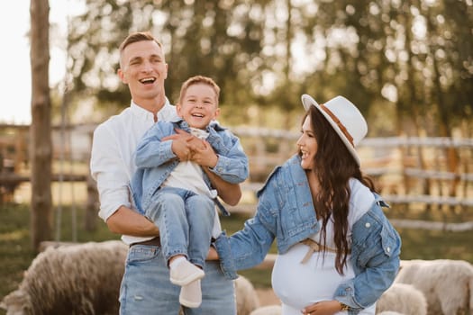 Stylish family in summer on a village farm with sheep.