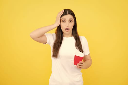 Close-up portrait of attractive dreamy girl holding in hands drinking latte isolated on yellow background. Young brunette woman drinking a cup of coffee