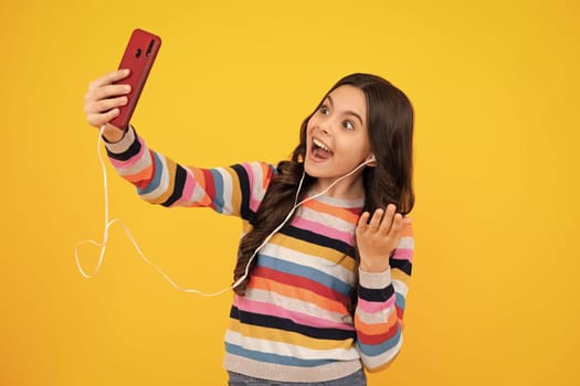 Kids selfie. Teenager girl use smart phone, share social media, chatting by mobile phone wear stylish casual trendy clothes isolated over yellow background. Smiling child with smartphone