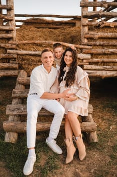 A stylish family in the countryside at sunset. A pregnant woman with her husband and son in nature.