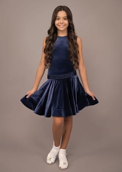 Happy girl face, positive and smiling emotions. Young graceful teenager child in fashion dress isolated on gray background. Beautiful teen in vogue trendy clothing