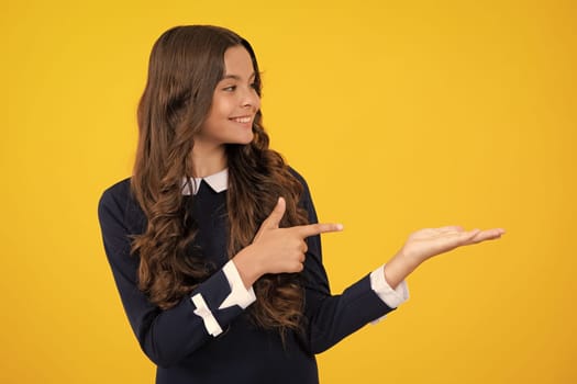 Close up portrait of teenager child girl showing at copy space, pointing to ads advertising, isolated over yellow background. Mock up copy space