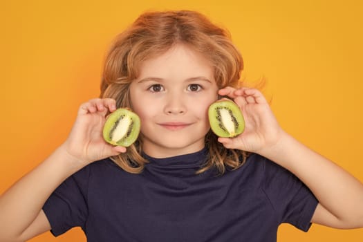 Child hold kiwi in studio. Kiwi fruit. Studio portrait of cute kid boy with kiwi isolated on yellow