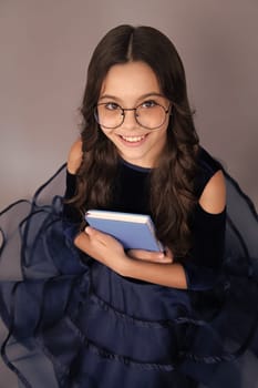 Happy smiling teenager school girl. Schoolchild, teenage student girl hold book on gray isolated studio background. School and education concept. Back to school