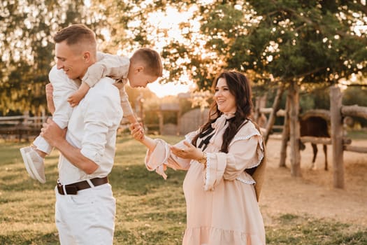 A stylish family in the countryside at sunset. A pregnant woman with her husband and son in nature.