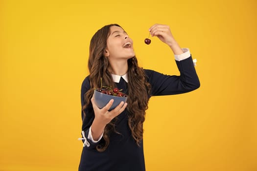 Teenager child girl eating cherries, isolated on yellow background. Summer berries, kids healthy cherry fruits