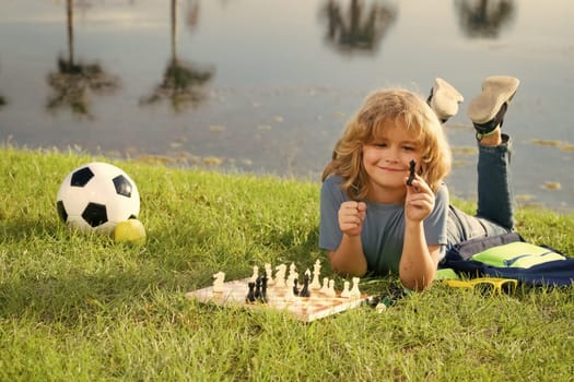 Concentrated kid developing chess strategy, playing board game in backyard, laying on grass