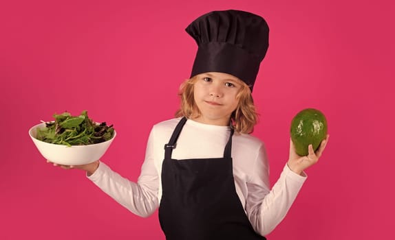 Kid cook with avocado and vegetable. Child in cook uniform. Chef kid isolated on pink background. Cute child to be a chef. Child dressed as a chef hat