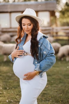 Stylish pregnant woman in a white hat in the countryside.