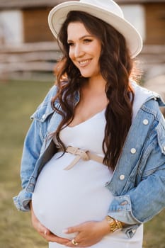 Stylish pregnant woman in a white hat in the countryside.