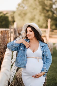 Stylish pregnant woman in a white hat in the countryside.