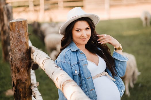 Stylish pregnant woman in a white hat in the countryside.