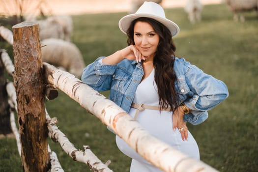 Stylish pregnant woman in a white hat in the countryside.