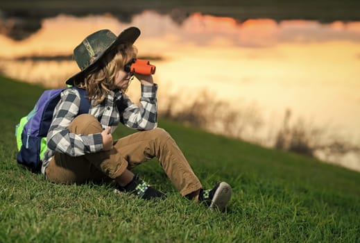 Young boy looking through binoculars. Little explorer. Outdoor recreation and adventures with kids. Child tourist on sunny countryside background