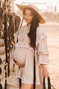 a pregnant woman in a dress and hat in the countryside holds a horse bridle in her hand.