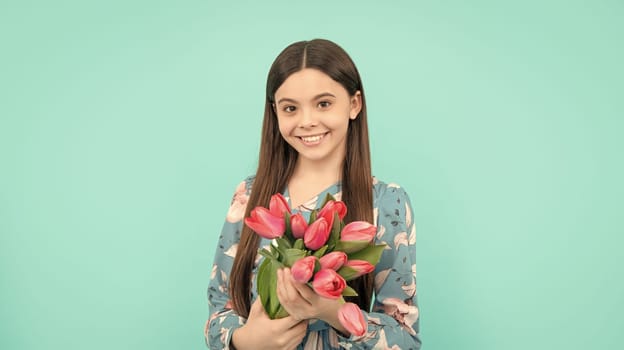 positive child with tulips. mothers or womens day. kid hold flowers for 8 of march. teen girl with spring bouquet on blue background. floral present. copy space.