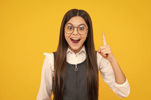 Excited face, cheerful emotions of teenager girl. Funny face of young teenager pointing up with finger, isolated on yellow background. Funny school girl, kid genius, nerd young student