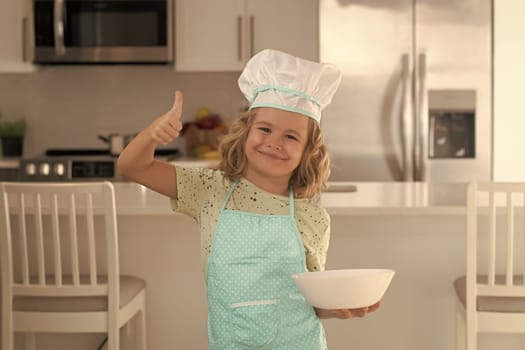 Child chef cook with cooking plate. Child chef cook is learning how to make a cake in the home kitchen. Child making tasty delicious. little boy in chef hat and an apron cooking in the kitchen