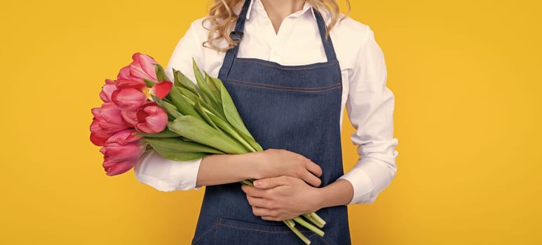 cheerful flower seller woman in apron with spring tulip flowers on yellow background.