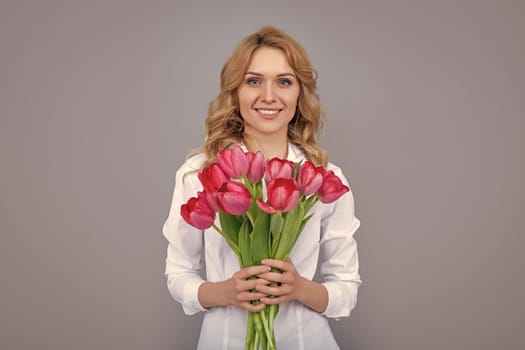 smiling blond woman with spring tulip flowers on grey background.