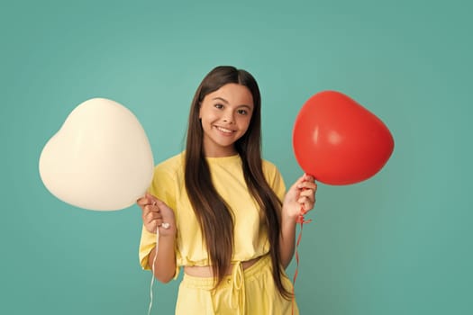 Valentines day and kids concept. Teenage girl in yellow dress with red heart-shaped balloon over blue background. Happy girl face, positive and smiling emotions