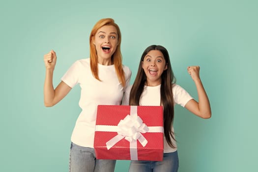 Mothers day. Excited amazed teen girl giving present to happy mother isolated on blue. Holidays christmas gift. Happy mother and daughter with gift box