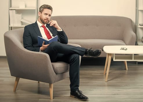 mature boss in suit sit in office making notes in notebook.