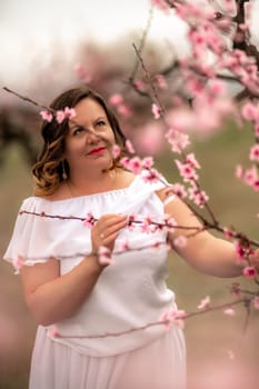 Woman peach blossom. Happy woman in white dress walking in the garden of blossoming peach trees in spring.