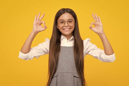 Okay. Beautiful child girl making ok sign on yellow background. Portrait of smiling kid show confident hands symbol. Teenager girl showing okey gesture. Happy girl face, positive and smiling emotions