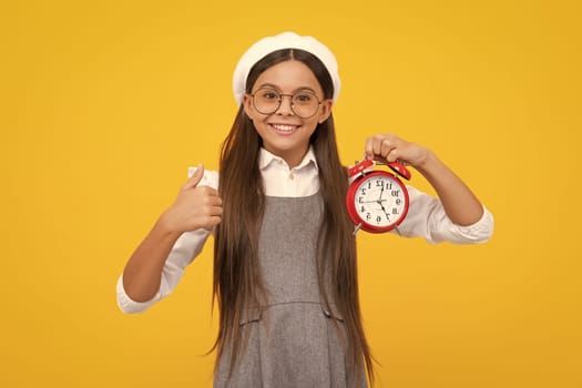 Teenager child hold clock isolated on yellow studio background. Teenager child with alarm clock showing time. Happy girl face, positive and smiling emotions