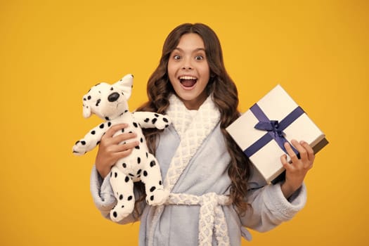 Teenager child holding gift box on yellow isolated background. Gift for kids birthday. Christmas or New Year present box. Amazed teen girl. Excited expression, cheerful and glad