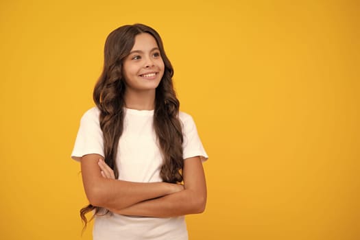 Confident child keep arms crossed, isolated on yellow background, empty space. Little caucasian teenage girl 12, 13, 14 years old hold hands crossed. Children studio portrait. Childhood lifestyle