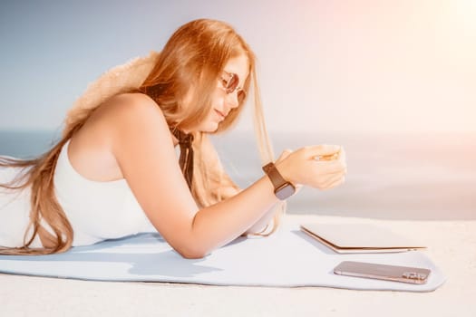 Successful business woman in yellow hat working on laptop by the sea. Pretty lady typing on computer at summer day outdoors. Freelance, travel and holidays concept.