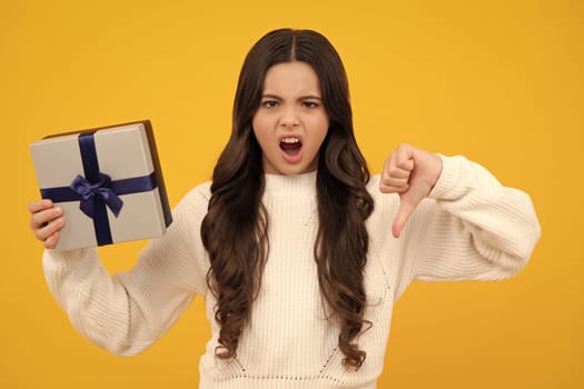 Angry face, upset emotions of teenager girl. Child teen girl with gift on yellow isolated background. Birthday, holiday present concept