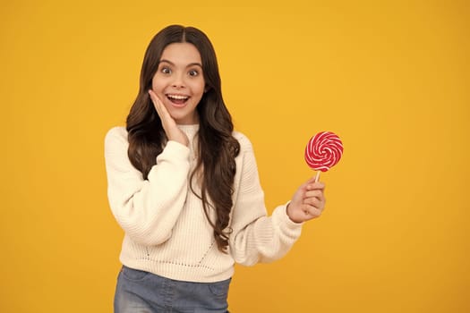Teen girl hold lollipop caramel on yellow background, candy shop. Teenager with sweets suckers. Happy face, positive and smiling emotions of teenager girl
