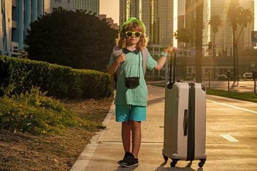 Child tourist with luggage travel bag travelling. Kid with suitcase walk on city street outdoor. Traveler tourist kid in casual clothes and hat hold suitcase