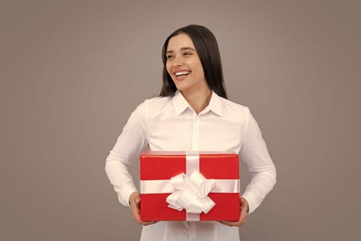 Portrait of a happy girl with gift box isolated over gray background. Woman holding gift present