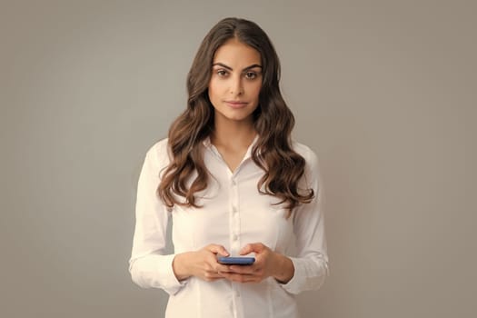 Serious businesswoman with smartphone, chat, sms concept. Isolated over gray background. Mobile offer. Girl chatting by mobile phone
